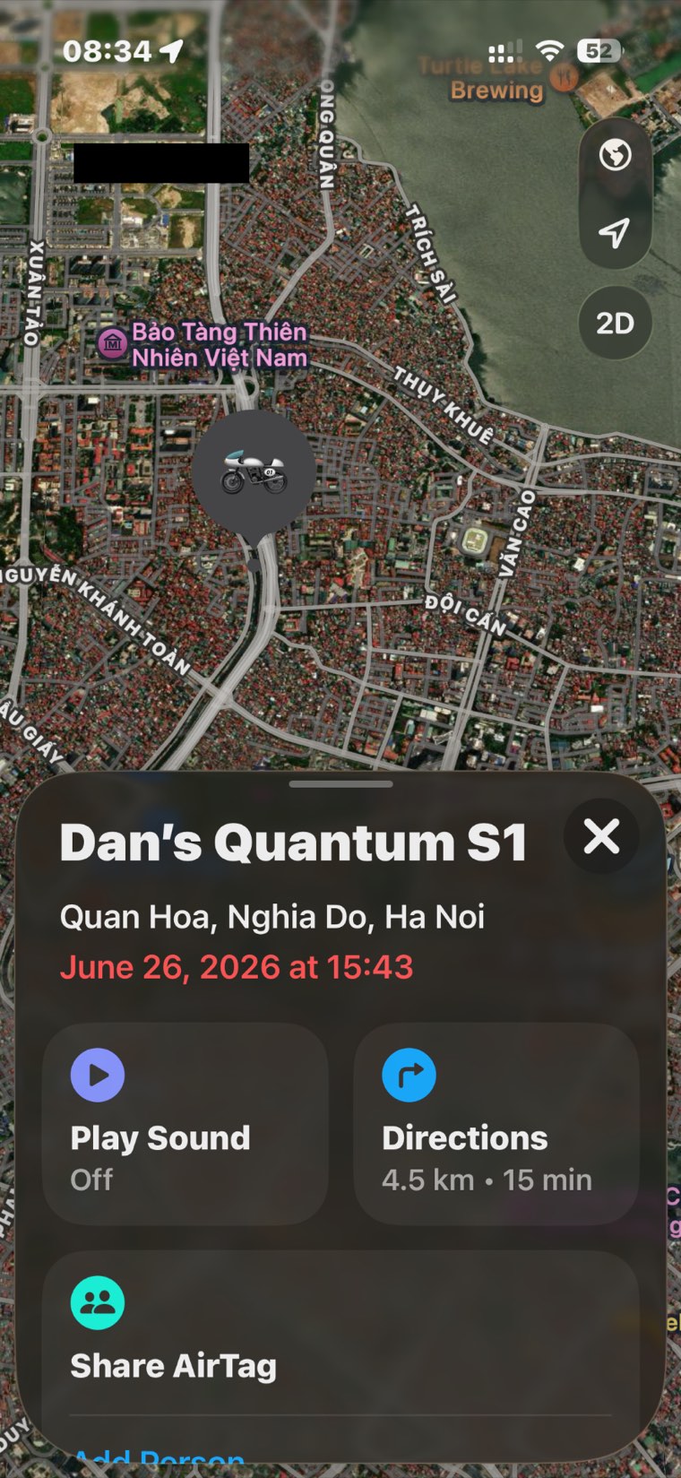 An iPhone Find My screen. A satellite map of Hanoi with a motorbike marker pinned over streets south west of West Lake, and one map label covered by a solid black redaction box. The panel below reads 'Dan's Quantum S1', then 'Quan Hoa, Nghia Do, Ha Noi', and in red 'June 26, 2026 at 15:43', above Play Sound, Directions and Share AirTag buttons.